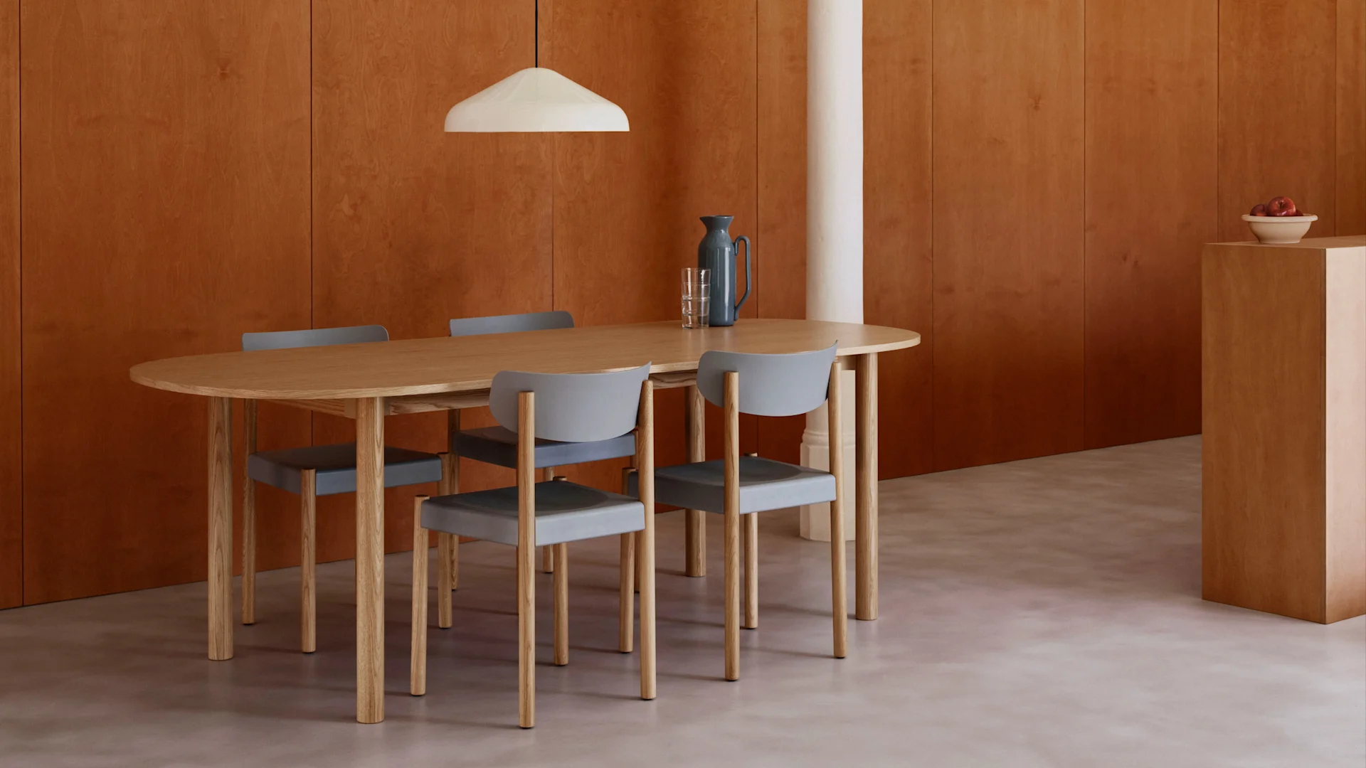 Modernes Esszimmer mit einem ovalen Holztisch, vier grauen Stühlen, warmen Holzpaneelen, hellem Boden und einer weißen Pendelleuchte.