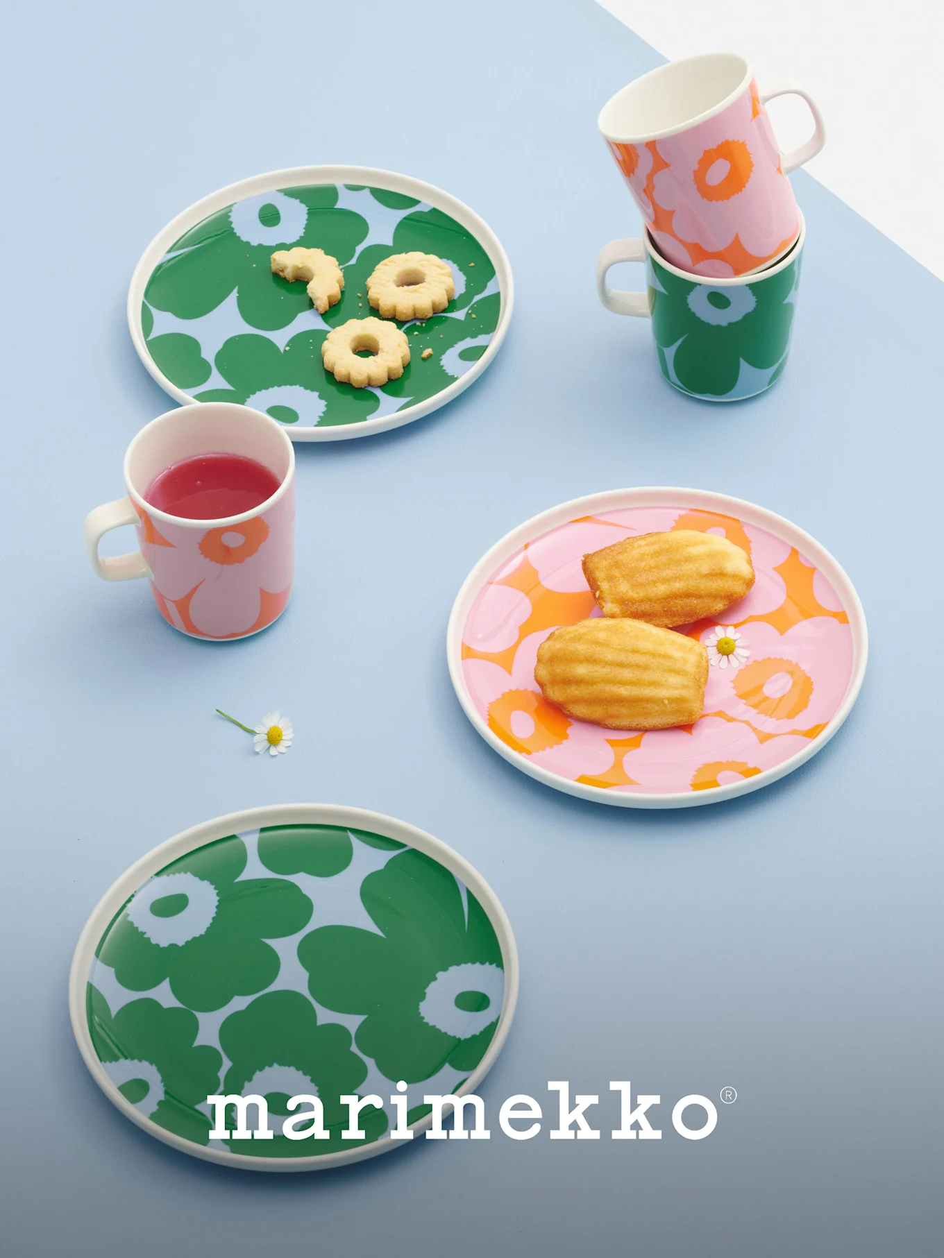 Marimekko Teller und Tassen mit kräftigen Blumenmustern in Grün, Pink und Orange, gefüllt mit Keksen, Madeleines und einem Getränk.