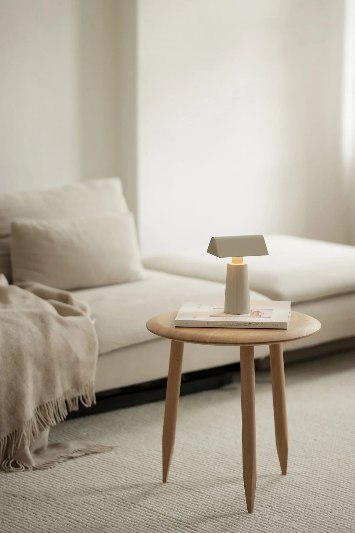 Der Lagom-Wohnstil zeichnet sich durch dezente Farben aus. Hier sehen Sie das beige Wohnzimmer von @b.wohnbar mit einer Couch und einem Beistelltisc davor, auf dem die Caret MF1 Tischleuchte von &Tradition steht.