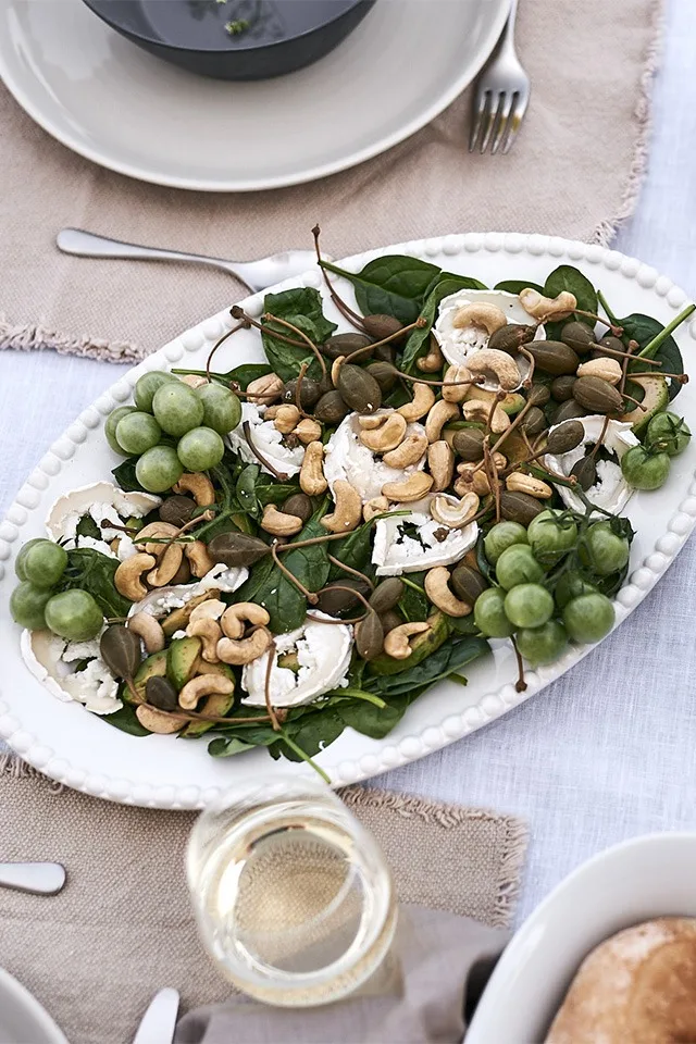 Ein vegetarischer Sommersalat mit Ziegenkäse, Babyspinat, Tomaten und Cashewnüssen, serviert auf einer ovalen Servierplatte von PotteryJo.