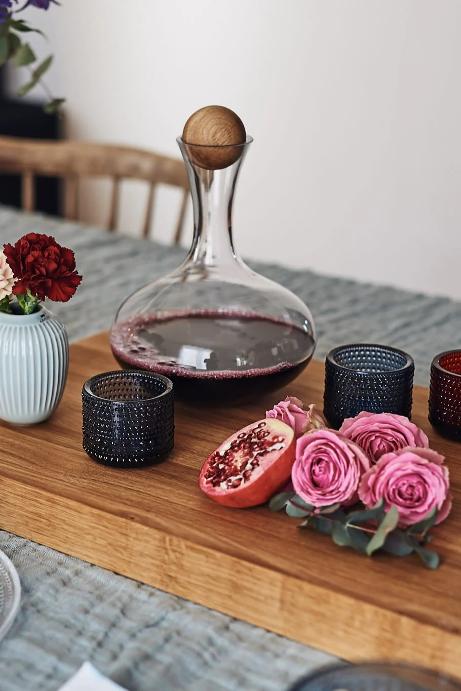 Ein romantisch gedeckter Tisch, bei dem ein großes hölzernes Schneidebrett von Global als Mittelstück dient, auf dem Windlichter von Iittala und eine Weinkaraffe stehen.