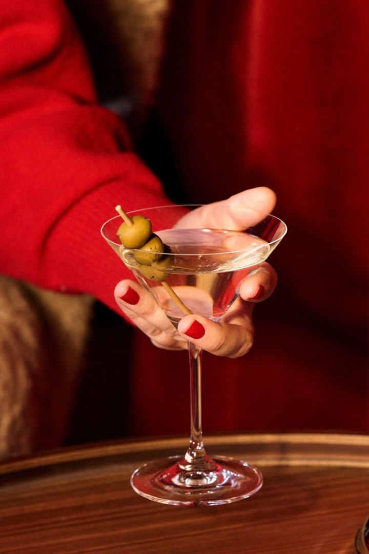 Verschiedene Arten von Cocktailgläsern: Welches Glas für welchen Cocktail? Hier sehen Sie eine Hand, welche das perfekte Glas für Martinis mit Oliven hält.