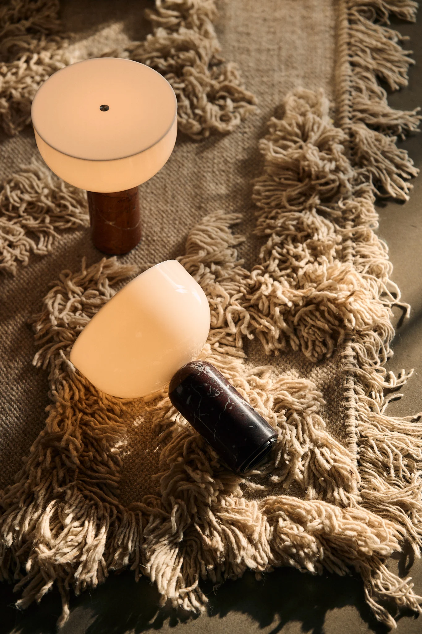 Auf einem Teppich liegen zwei skandinavische Lampen - die Kizu Tischleuchten von New Works.