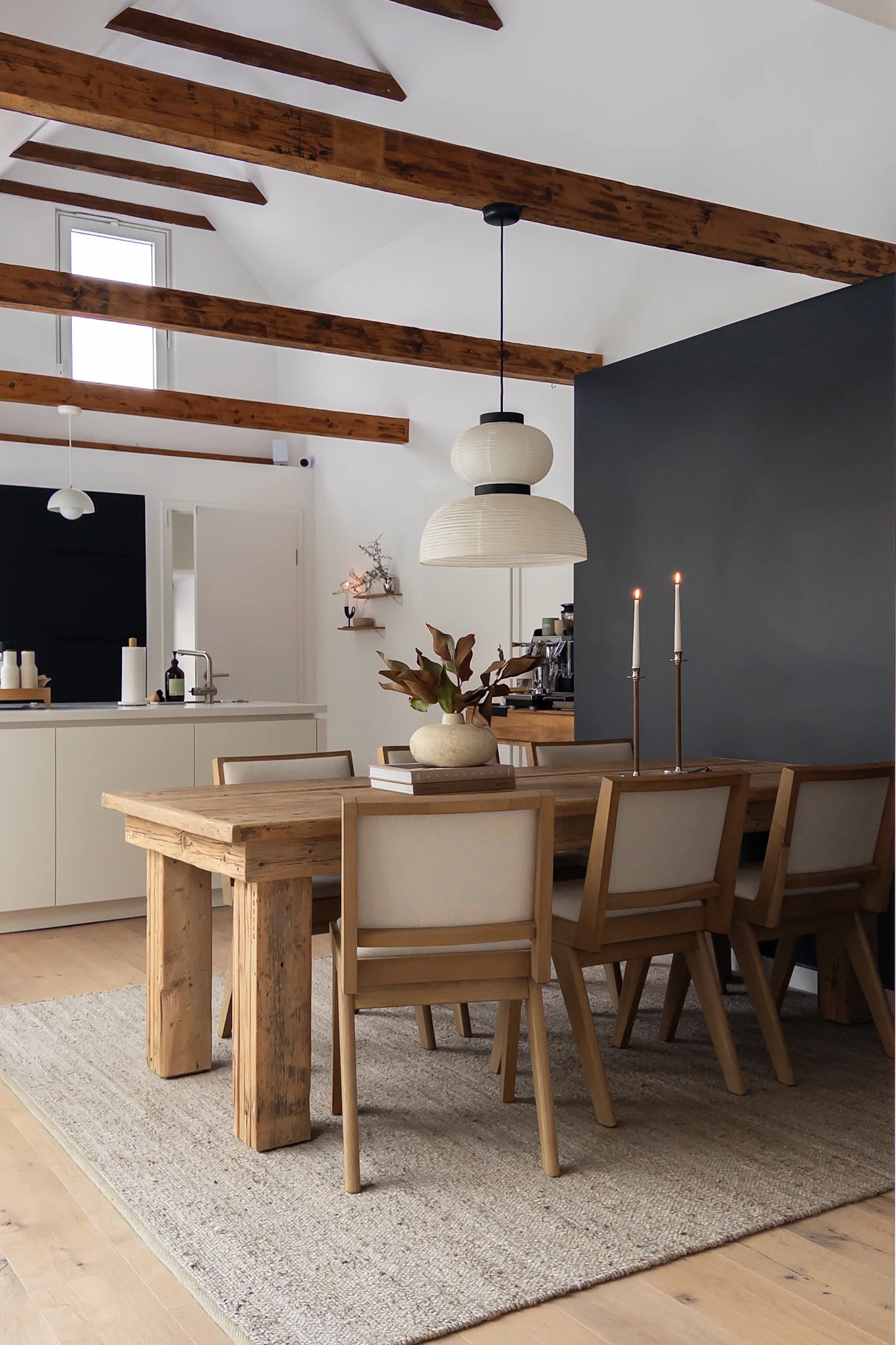 Ein stilvolles Esszimmer mit einem rustikalen Holztisch, sechs gepolsterten Stühlen, einer zweistufigen Papierlaternenlampe und Kerzen.