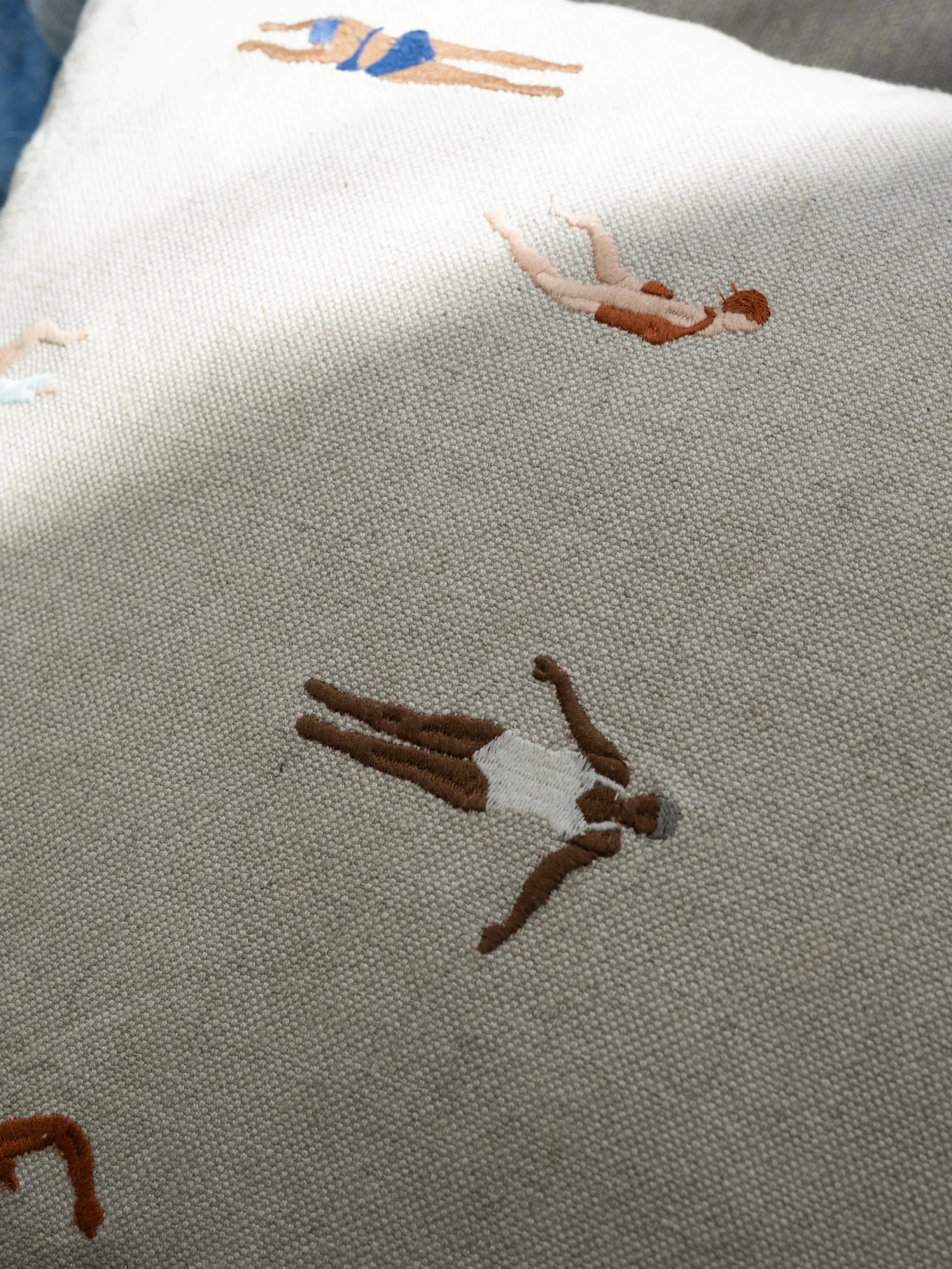 Hellfarbiger bestickter Stoff mit stilisierten Schwimmern in verschiedenen Hauttönen und Badebekleidung.