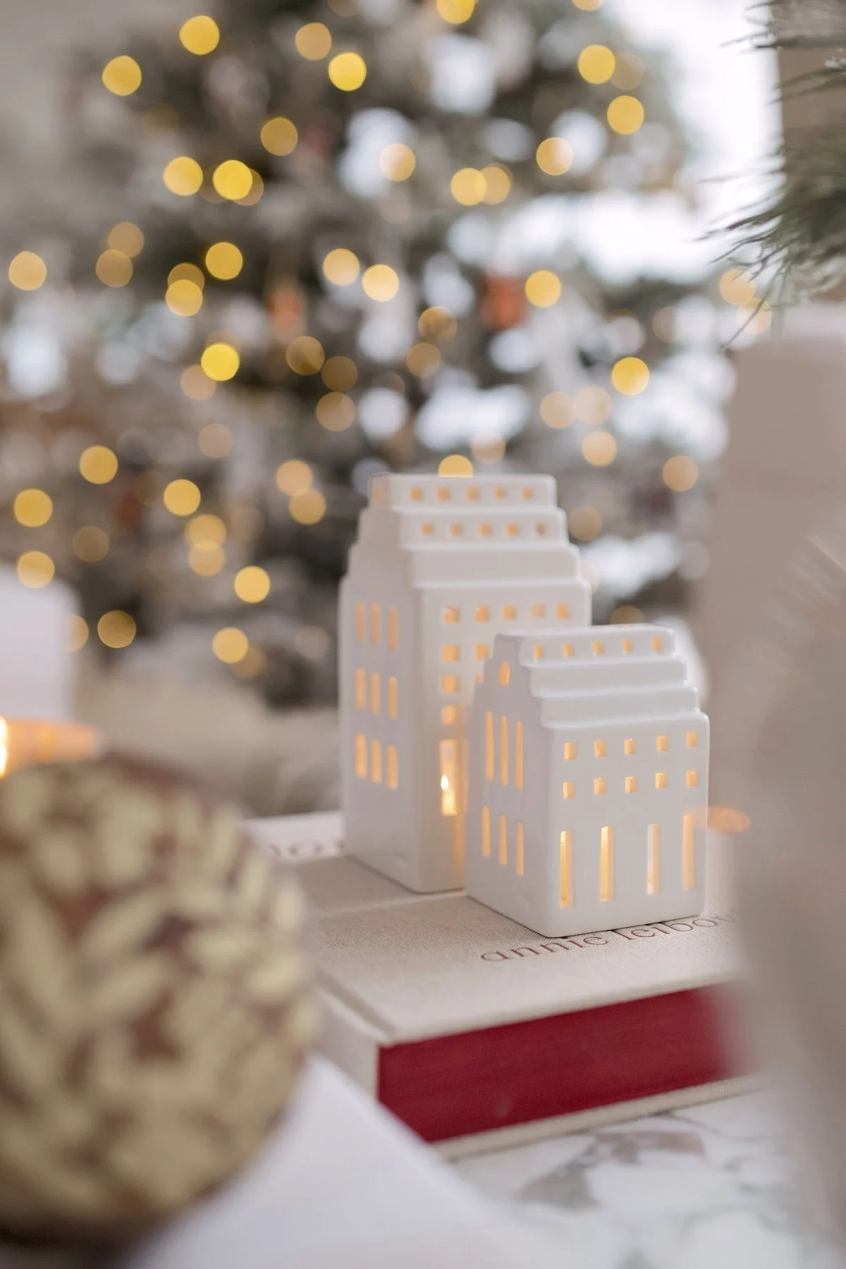 Deux maisons lumineuses de la collection Urbania de Kähler sont posées sur un livre devant un sapin de Noël, chez @widveyshome.