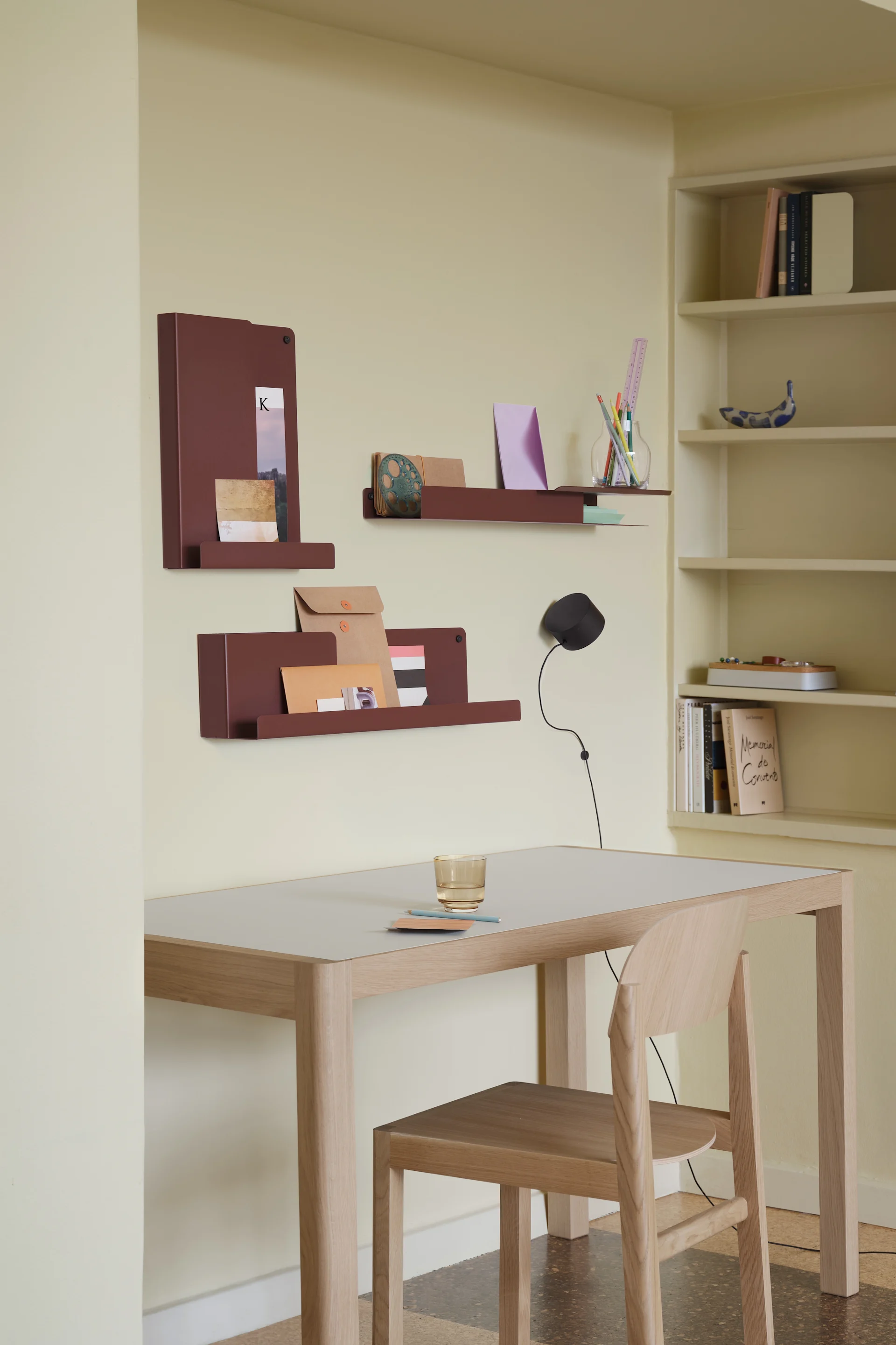 Heimbüro mit hellem Holzschreibtisch und Stuhl, rotbraunen Wandregalen und einem Bücherregal.