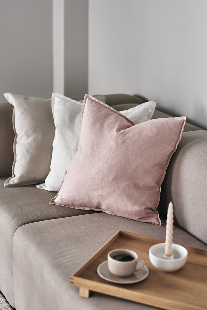 Lassen Sie sich in fluffige Kissen sinken und genießen Sie Ihren Mittagskaffee – hier Kissenüberzüge, Freckle Tasse mit Untersetzer und Valley Kerzenhalter in Weiß von Scandi Living und dem Holztablett von Ferm Living.