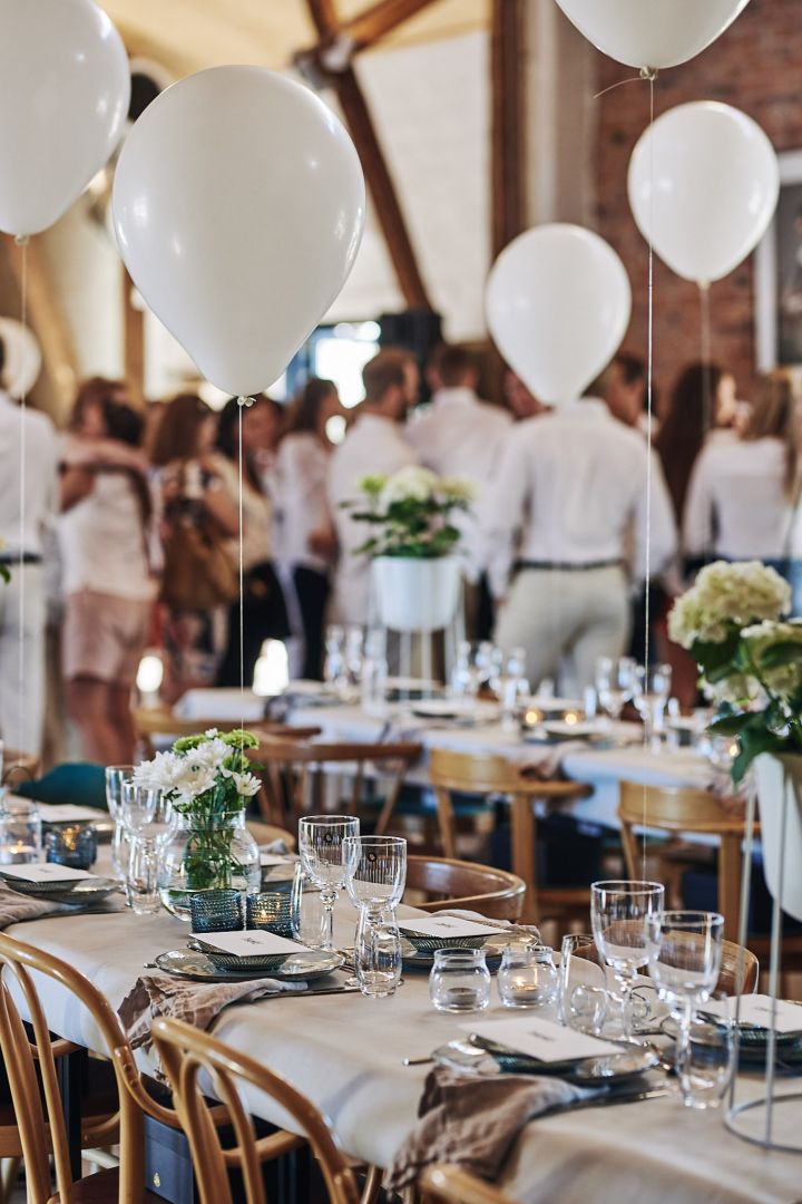 Lange Tische sind für ein Sommerfest in Weiß eingedeckt, während Luftballons über den Tischen schweben. 