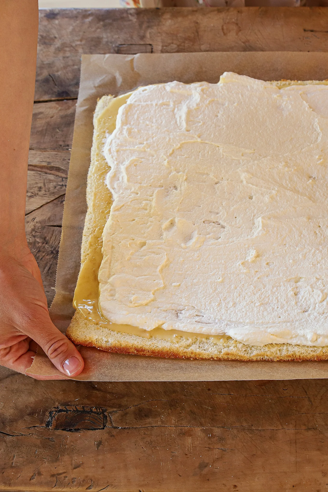 Der Biskuitteig wird mit Zitronencreme und Sahne bestrichen.