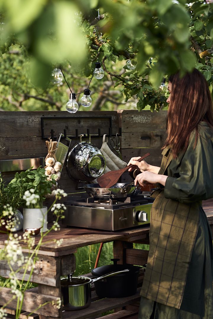 Outdoor Küche selber bauen: Hier sehen Sie eine Frau, welche in Ihrer aus Paletten bestehenden Outdoor-Küche am Kochen ist.