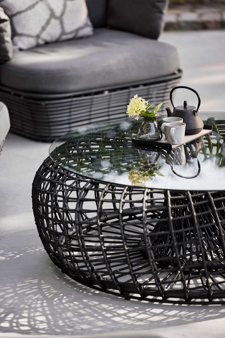 Der Nest-Tisch von Cane-line in Schwarz besteht aus Glas und Aluminium und besticht mit seiner runden Form - definitiv ein Gartenmöbel-Trend 2025.