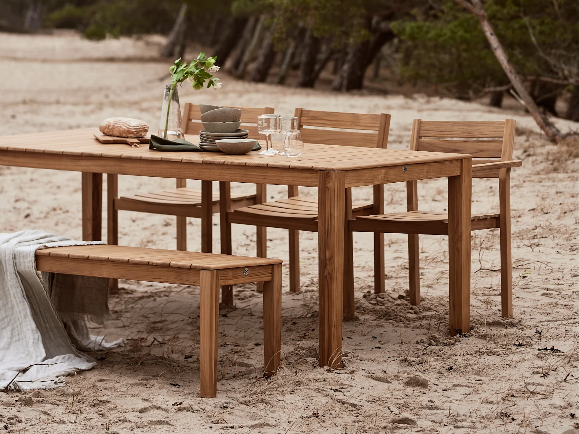 Hölzernes Outdoor-Essset mit Tisch, Stühlen und Bank, dekoriert mit Geschirr und Decke am Sandstrand.