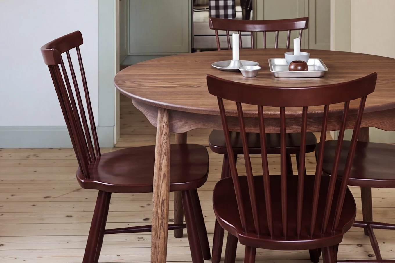 Esszimmer mit rundem Holztisch, roten Stühlen und einer roten Pendelleuchte, blickt in eine Küche mit hellgrünen Schränken.