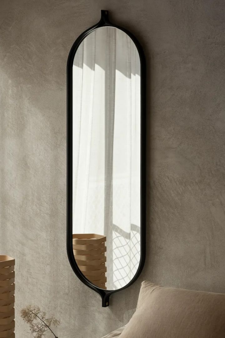 Der Comma Spiegel in schwarzer Esche hängt neben einem Bett der schwedischen Möbelmarke Swedese. 