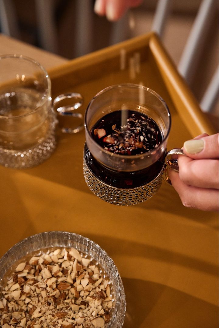 Schwedisches Weihnachtsessen: Eine Hand streut Mandeln in ein traditionelles Glas mit Glögg auf einem nordischen Weihnachtstisch. 