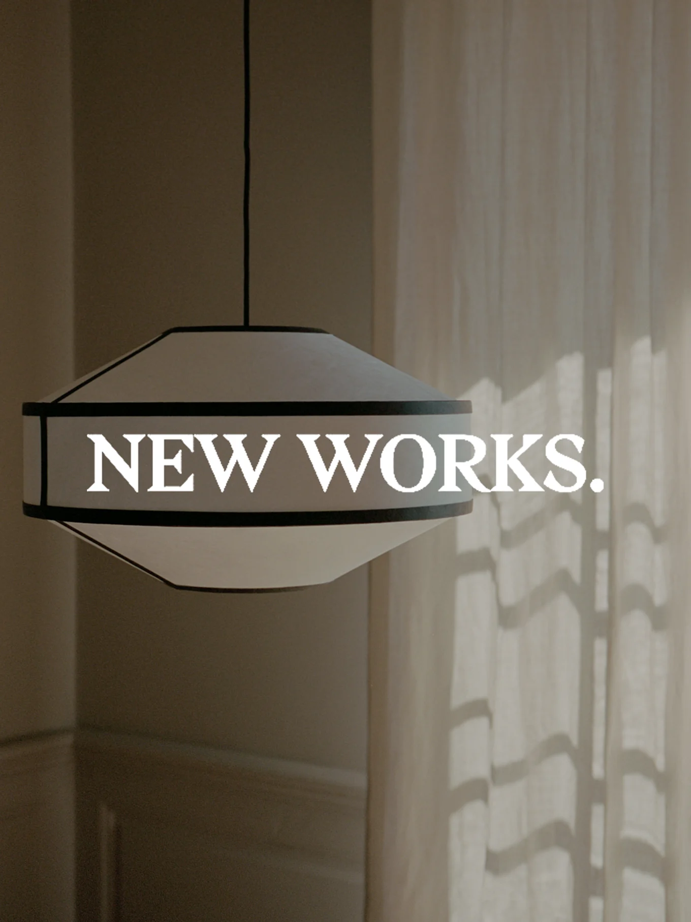 Eine breite, weiße Pendelleuchte mit dunklem Rand hängt, mit dem Text 'NEW WORKS.' überlagert. Sonnenlicht wirft Schatten auf einen Vorhang.