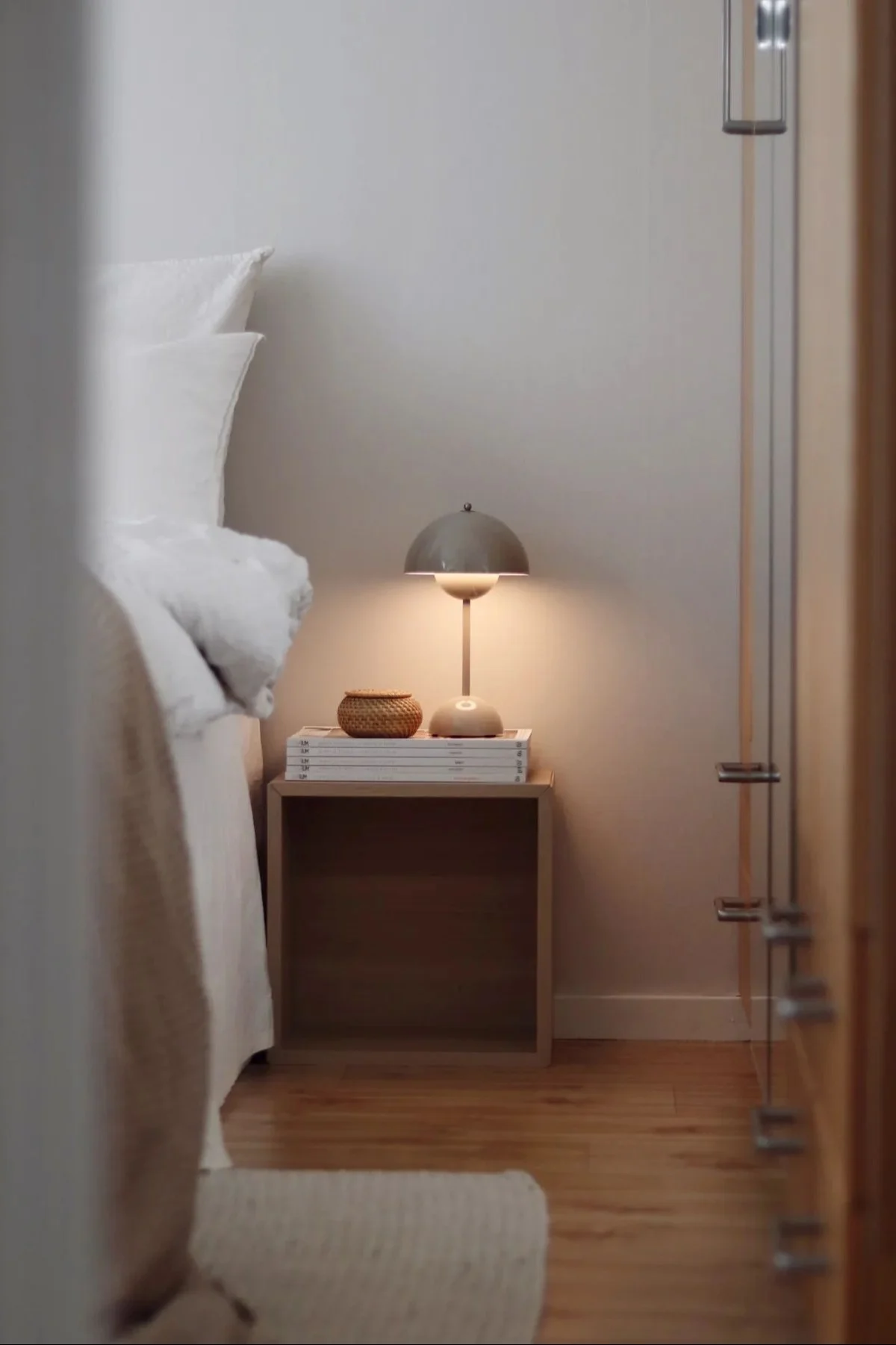 Die Akku-Tischleuchte Flowerpot von &tradition steht leuchtend neben einem Bett.