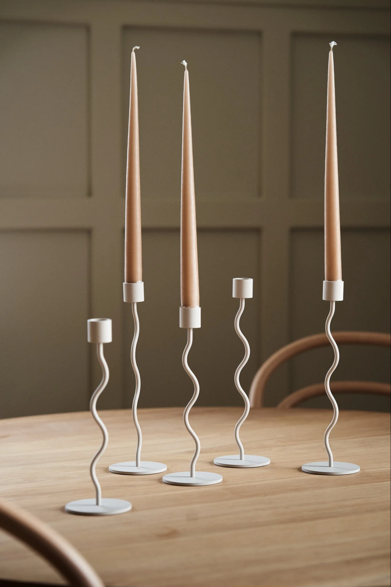 Eine Kollektion des Curved Kerzenhalters in Beige von Cooee Design auf einem hölzernen Esstisch. 