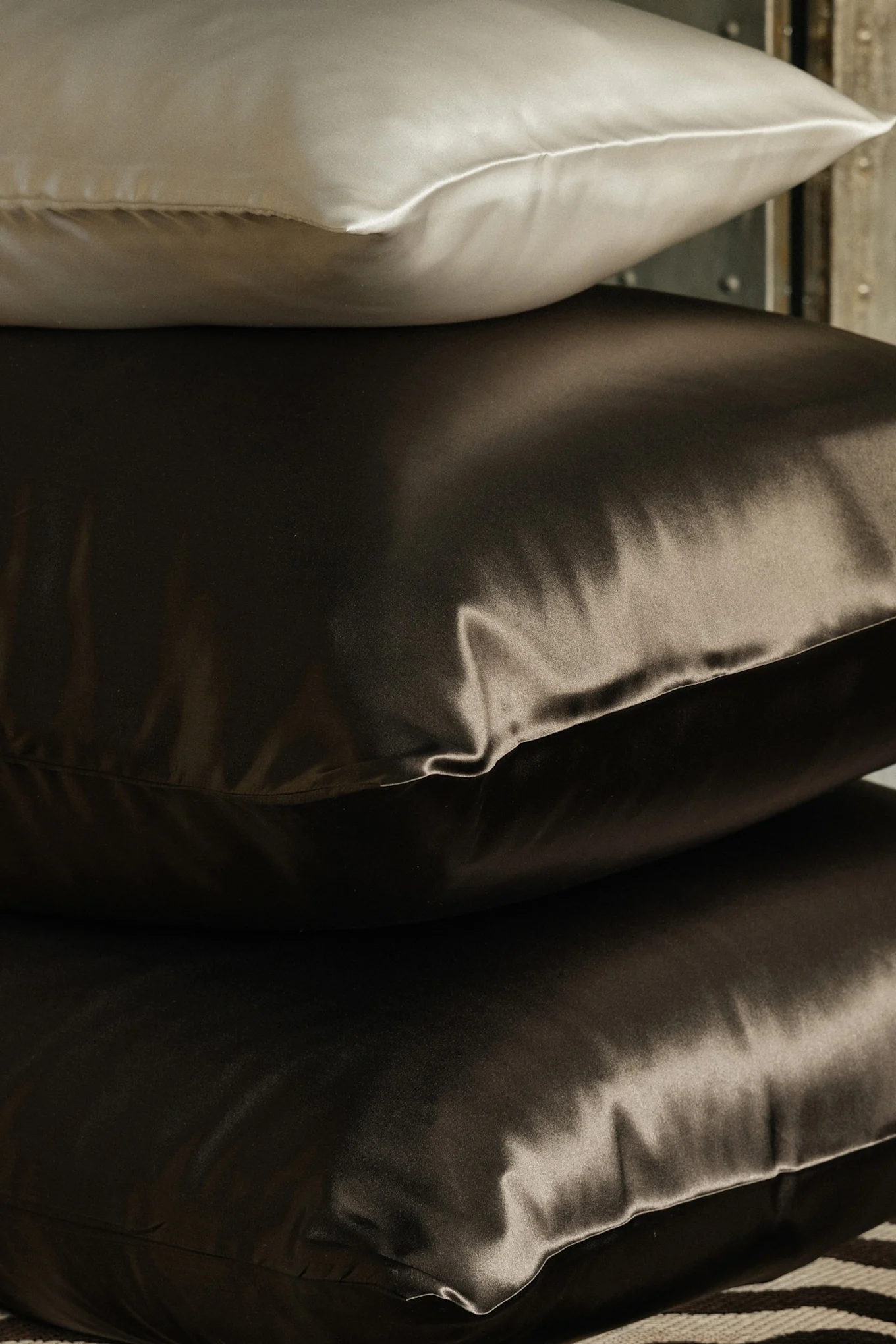 Stapel von drei Seidenkissen, eines hell und zwei dunkelbraun.