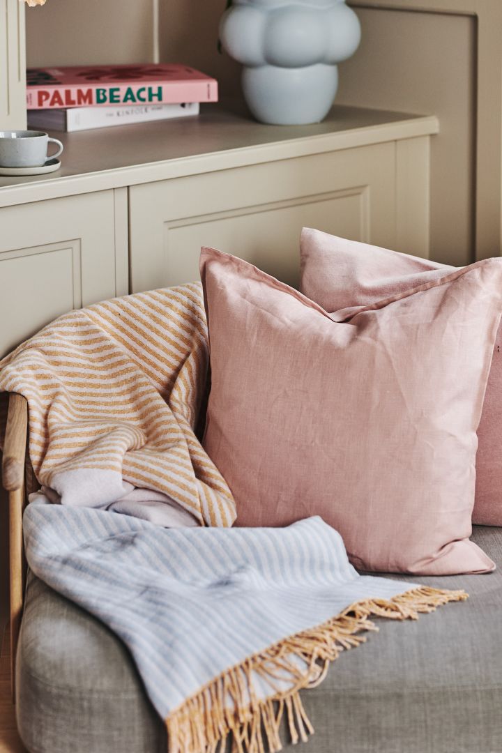 Bringen Sie Pastellfarben in Ihr Interieur, indem Sie mit der Baumwolldecke Stripes von NJRD in Gelb-, Orange- und Blautönen zusammen mit dem Kissen Calm in Dusty Rose von Scandi Living dekorieren.