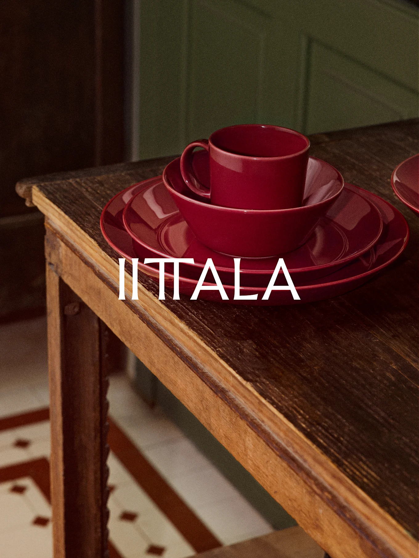 Ein Stapel rotes IITTALA Geschirr, bestehend aus Tasse, Schale und Tellern, steht auf einem rustikalen Holztisch.