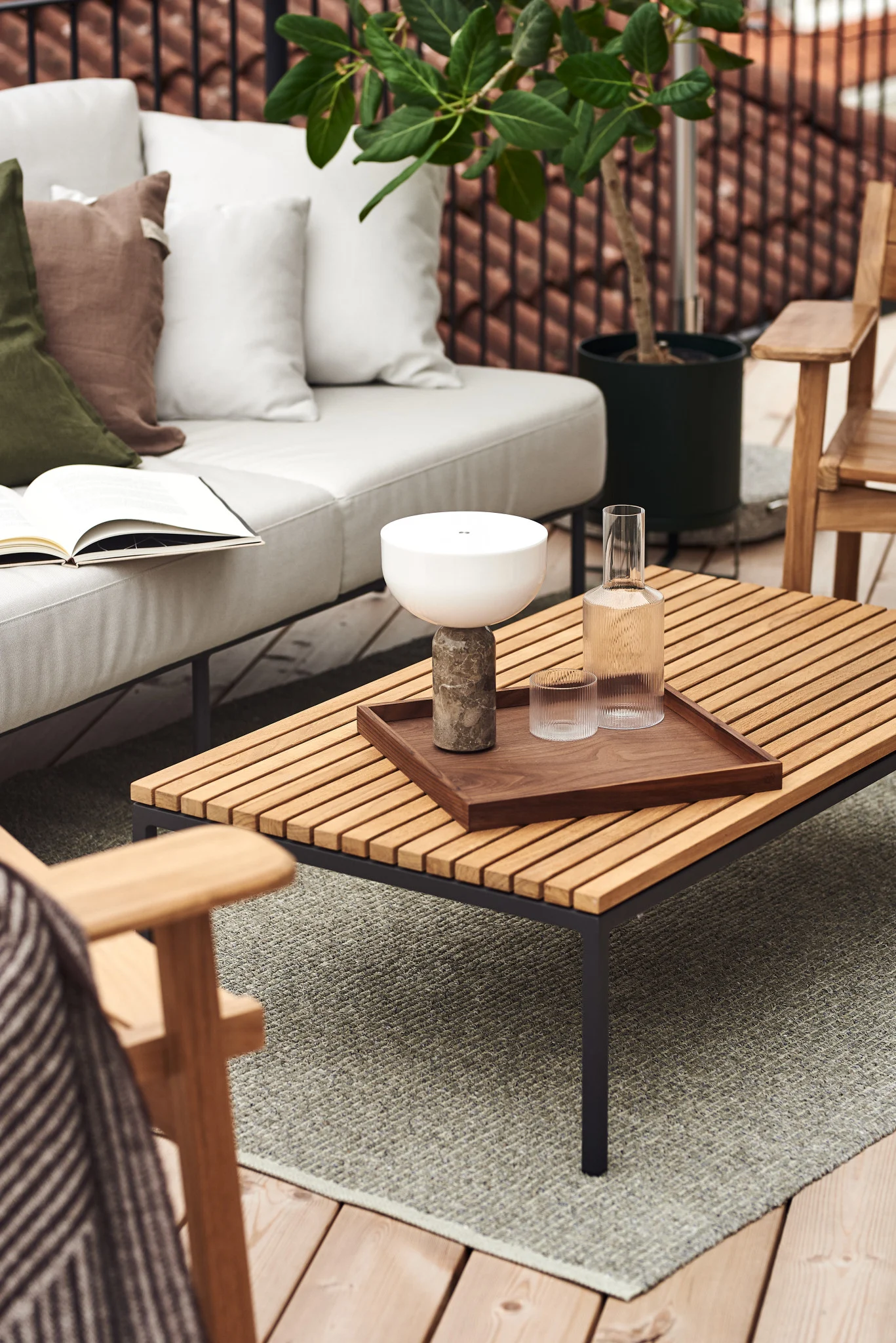Auf einem Outdoor-Tisch auf einem Balkon stehen die Kizu Tischleuchte und eine Ripple Karaffe.