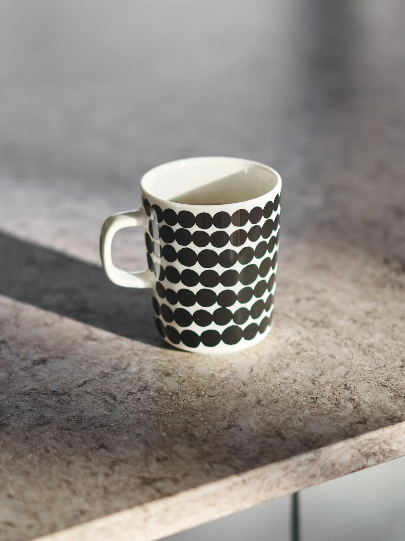 Weiße Keramiktasse mit schwarzen Polka-Dots auf einer grauen Arbeitsplatte.