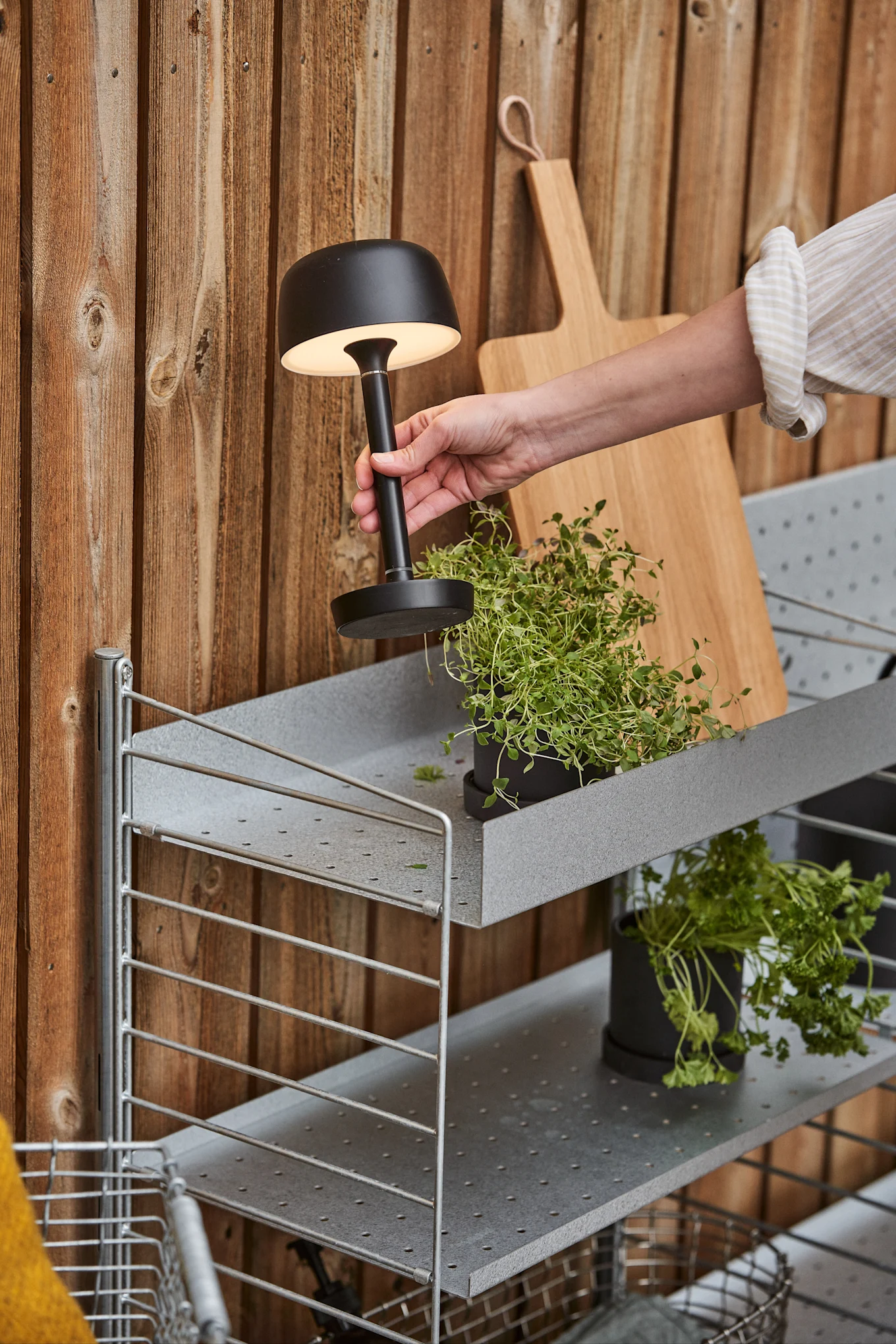 Die schwarze Akku-Tischleuchte Halo von Scandi Living wird im Freien auf einem Regal platziert.