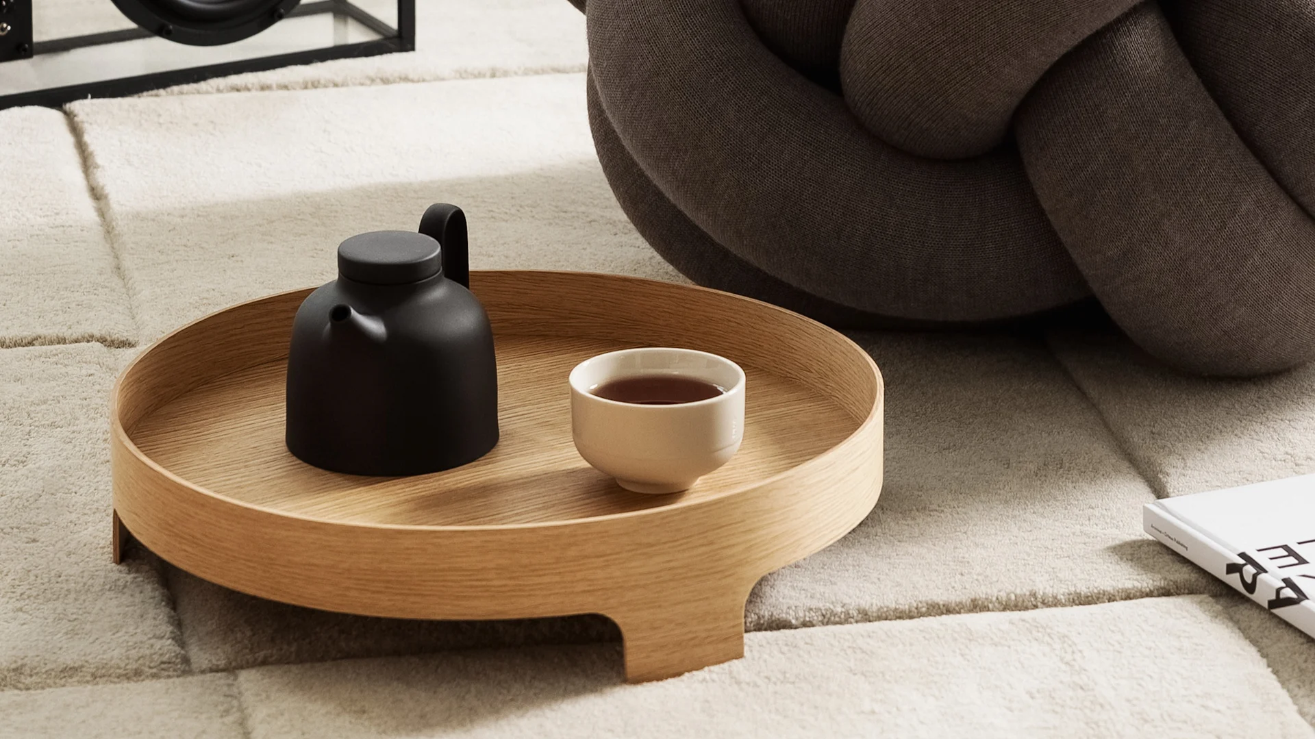 Lagom: Das Bridge Tablett steht auf einem Teppich, darauf eine Teekanne und eine Teetasse, im Hintergrund das XL Kissen, alles von Design House Stockholm.