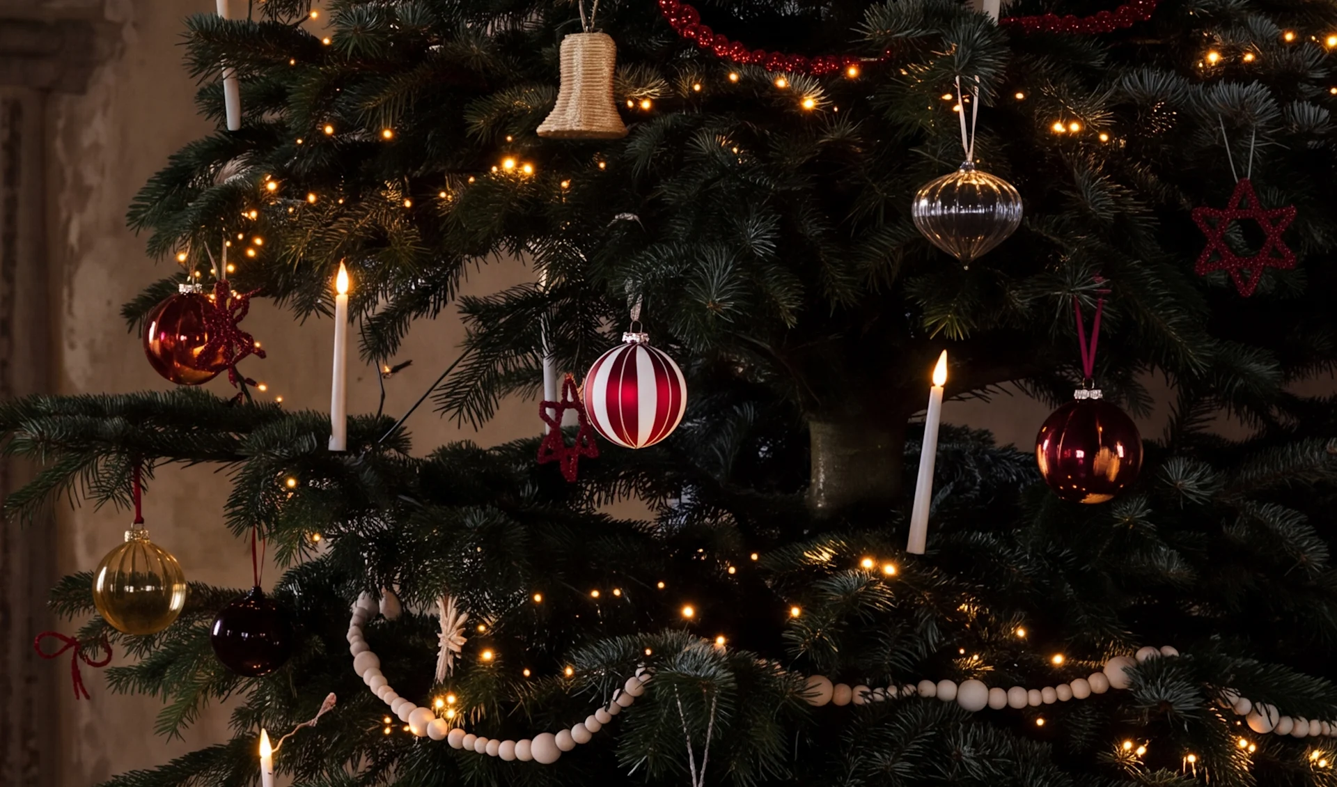 Ein geschmückter Weihnachtsbaum mit warmen Lichtern, roten, silbernen und goldenen Kugeln, weißen Kerzen und Holzperlengirlanden.