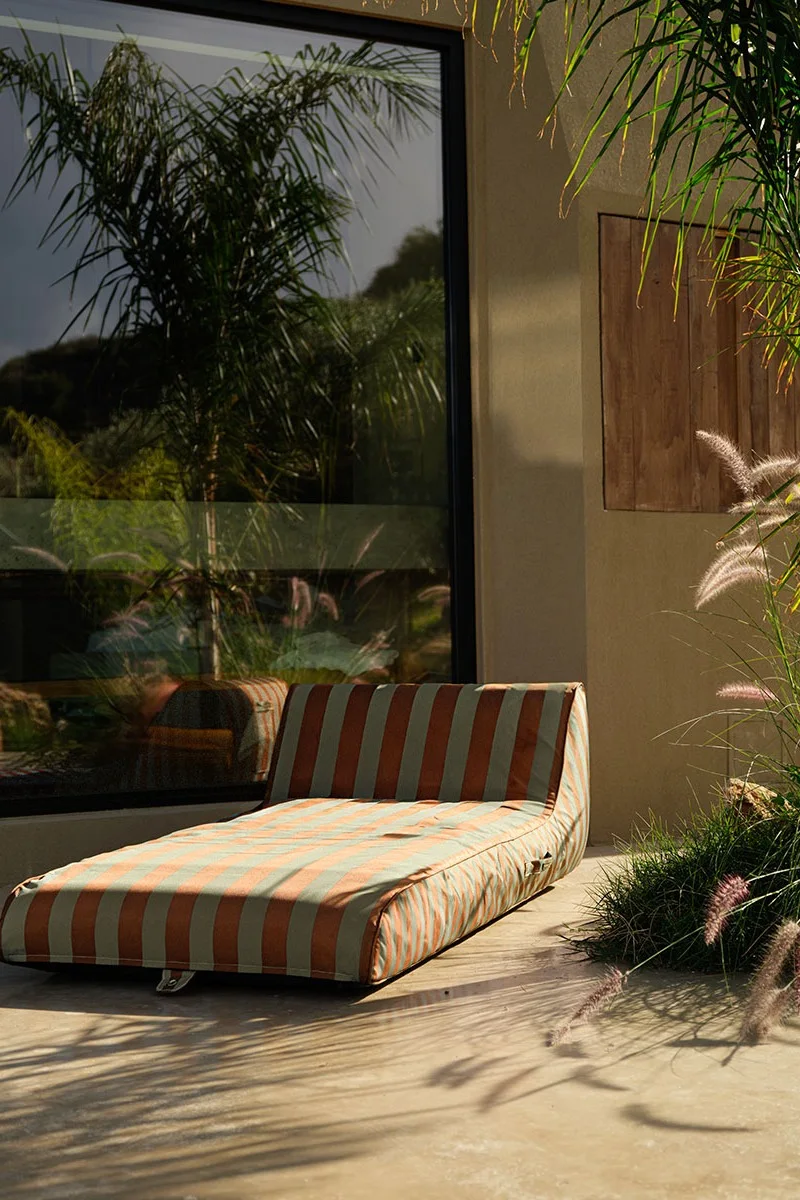 Gestreifte Chaiselongue auf einer Terrasse mit großem Fenster, das Palmen reflektiert.
