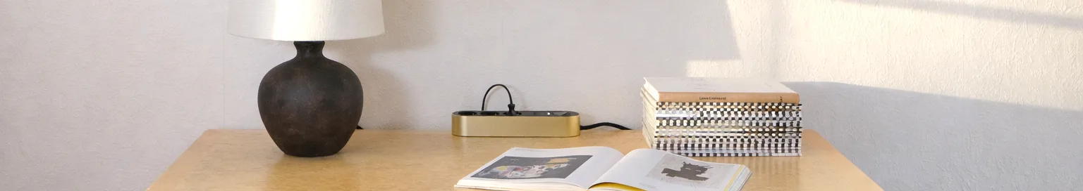 Goldfarbene Steckdosenleiste mit drei schwarzen Steckdosen und einem Netzschalter auf hellem Untergrund.