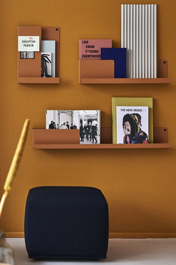 Orangefarbenes folded Regal von Muuto vor einer gleichfarbigen Wand mit dunkelblauem Sitzkissen. 