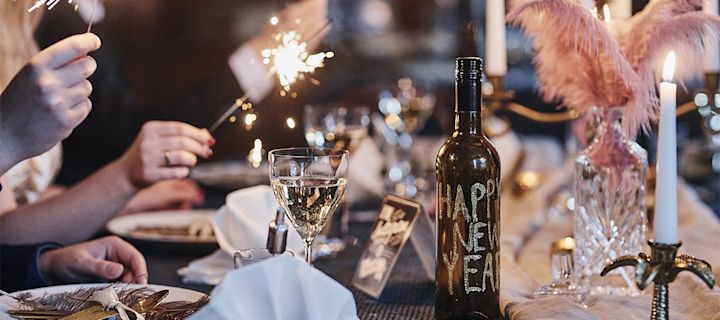 Ideen für Ihre Silvesterparty: Hier sehen Sie eine mit Glitzerschrift verzierte Flasche auf einem elegant gedeckten Tisch stehen.