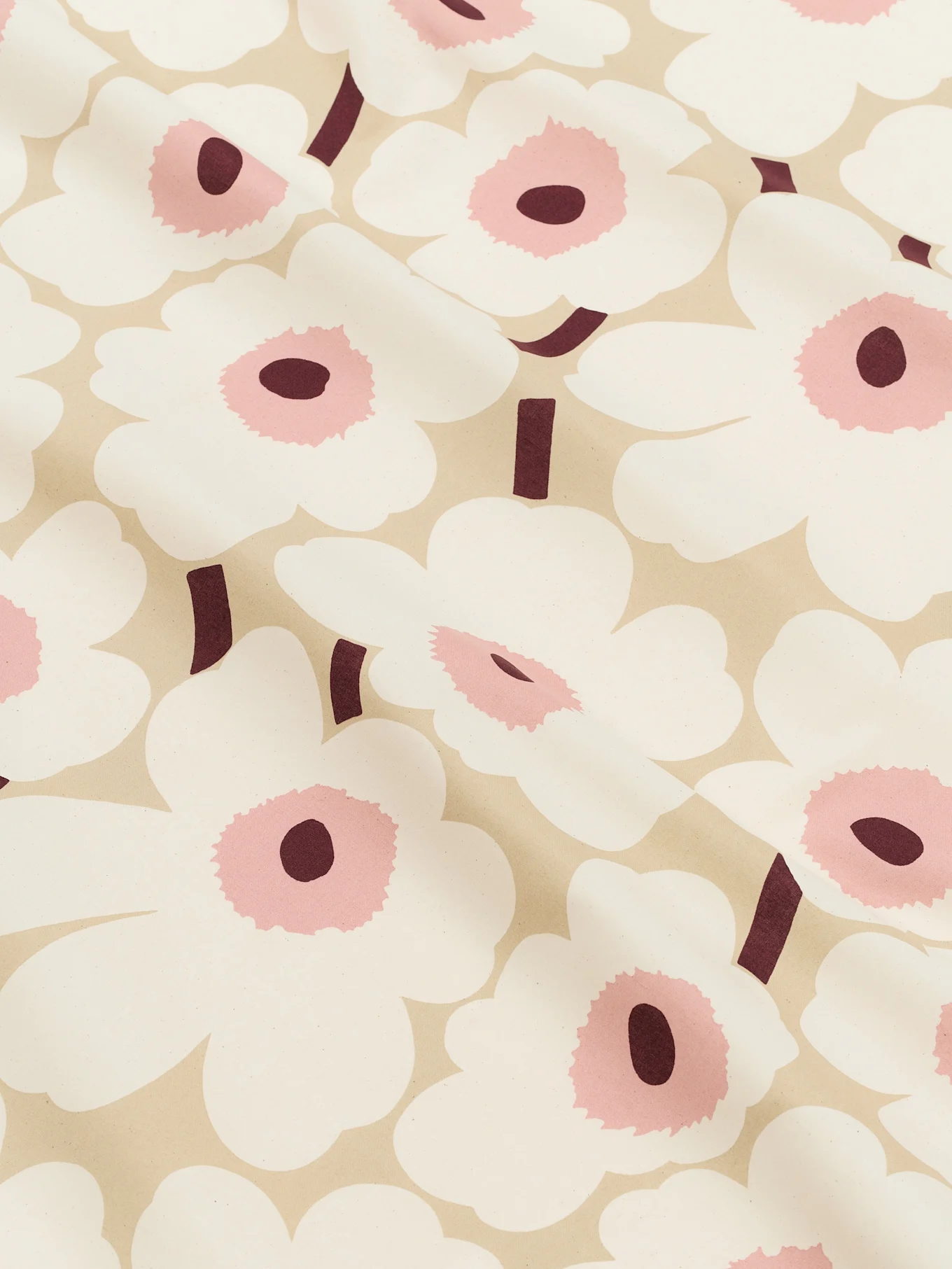 Nahaufnahme eines hellbeigen Stoffes mit einem Muster aus großen weißen stilisierten Blüten mit rosa Zentren und dunkelroten Stielen.