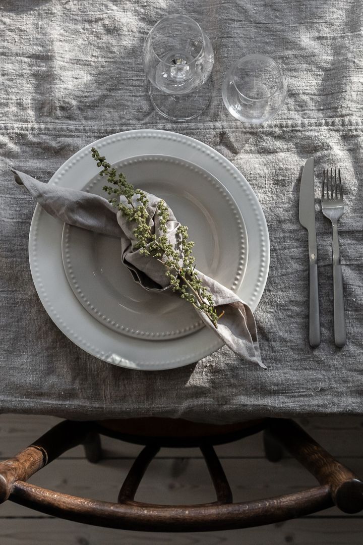Tipps zum Falten von Servietten mit einer geknoteten Leinenserviette, die auf Tellern von Scandi Living liegt.