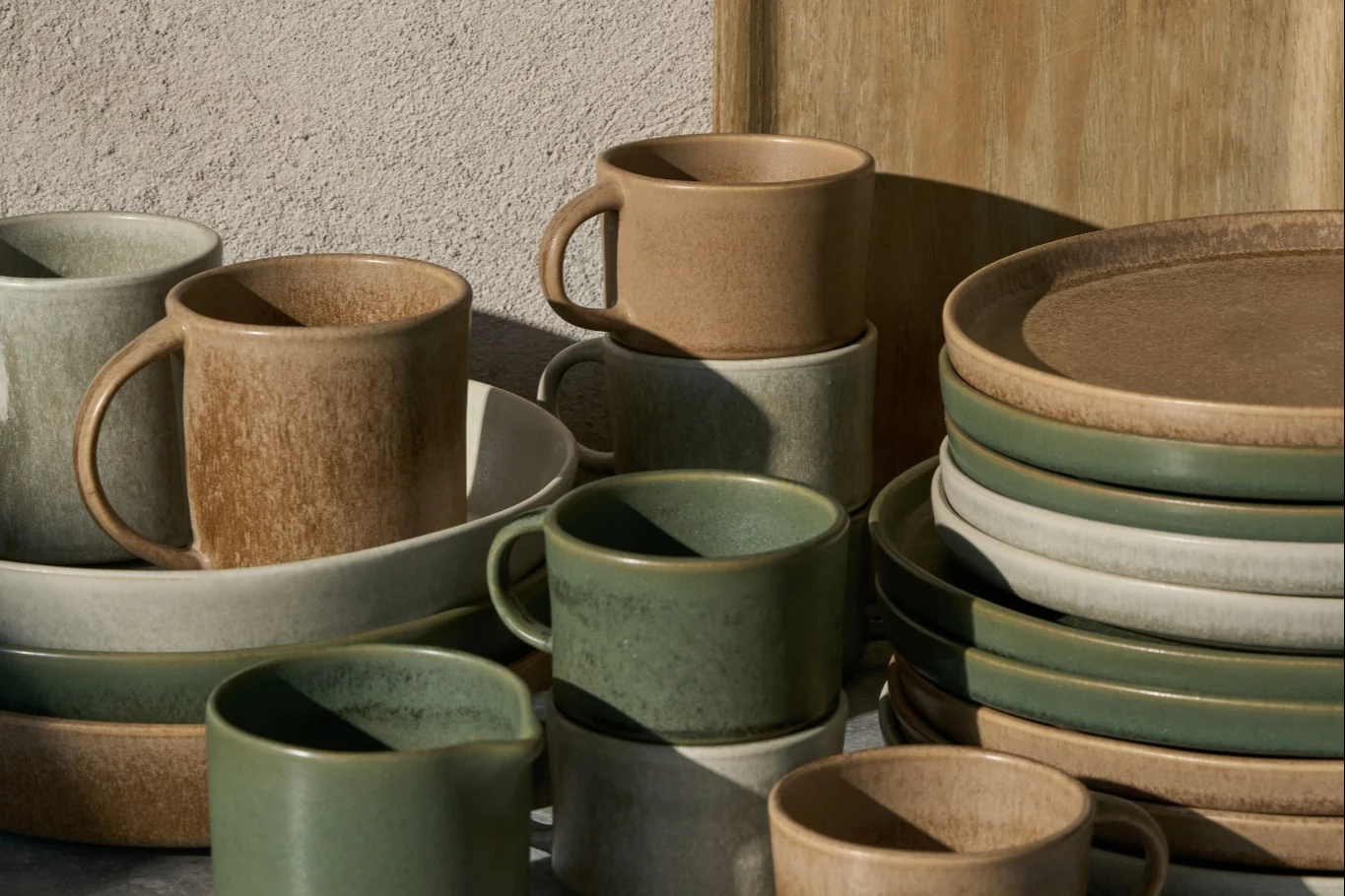 Gestapelte Keramikbecher, Schalen und Teller in Beige, Hellgrau und Salbeigrün mit rustikalem Finish.