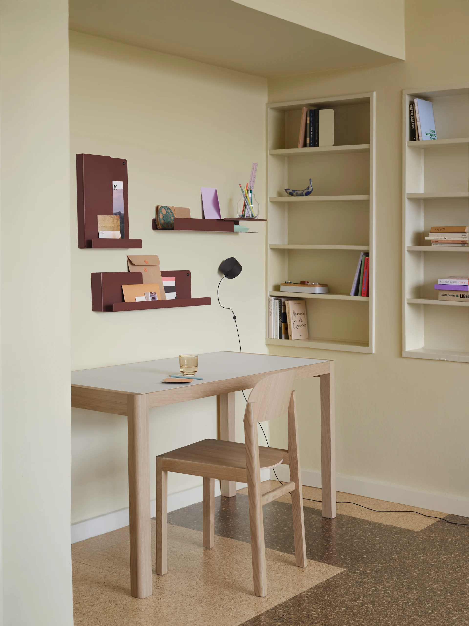 Eine minimalistische Büroeinrichtung mit hellem Holzschreibtisch, Stuhl, rotbraunen Wandorganisatoren und eingebauten Bücherregalen.