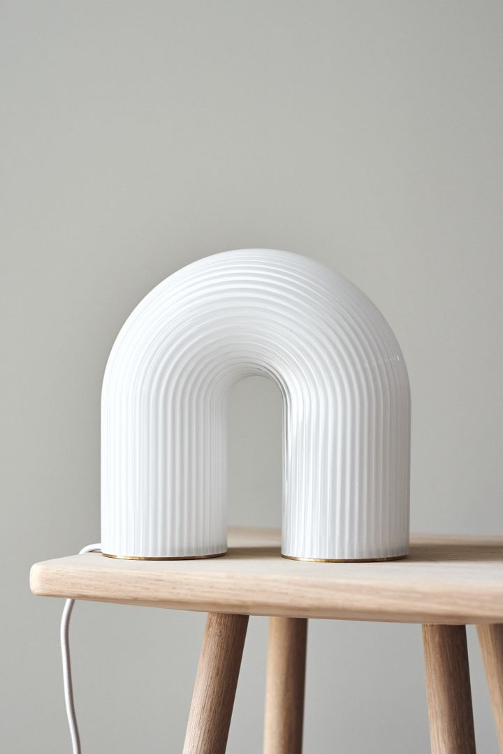 Beleben Sie Ihr Zuhause mit moderner Beleuchtung – hier sehen Sie die verspielte Vuelta Tischleuchte in Weiß von Ferm Living auf einem kleinen Hocker aus Holz. 