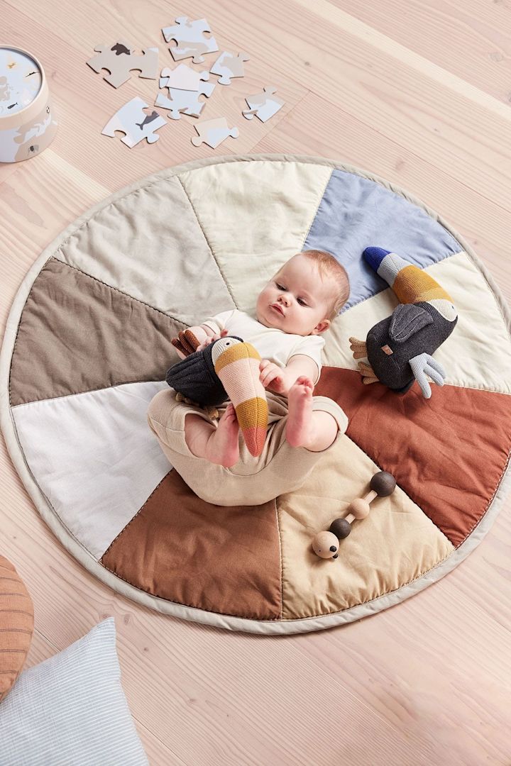 Das Trine Tourca Plüschtier von OYOY liegt neben einem Baby auf dem Moni Kinderteppich. Das Plüschtier besteht ausschließlich aus recycelten Materialien und macht es damit nicht nur zu einem tollen, sondern auch zu einem nachhaltigen Geschenk zur Babyparty.