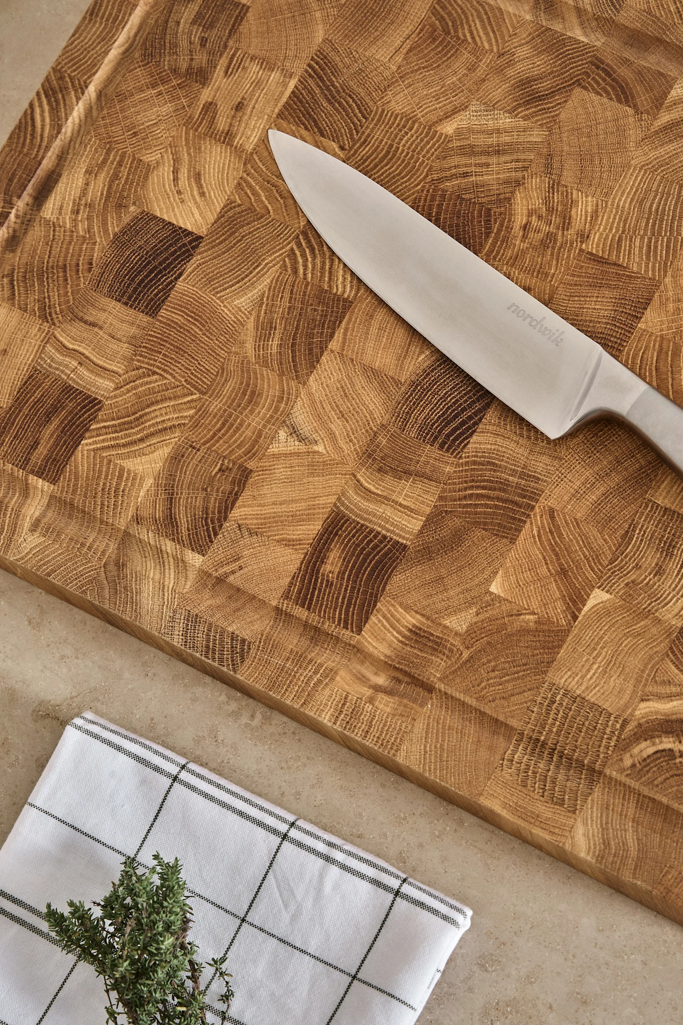 Nordwik Kochmesser auf einem Holzschneidebrett mit Stirnholzmaserung, kariertem Handtuch und frischem Thymian.