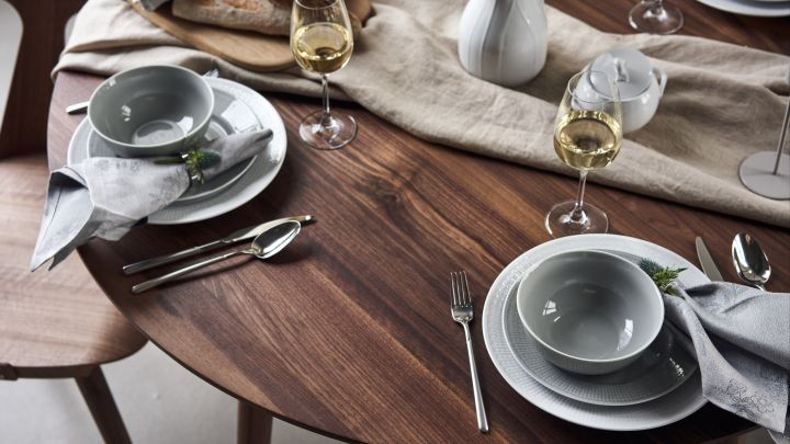 Ein festlich gedeckter Tisch mit Swedish Grace-Porzellan in Weiß und Grau mit Leinenservietten von Rörstrand und weißen Weingläsern von Scandi Living. 