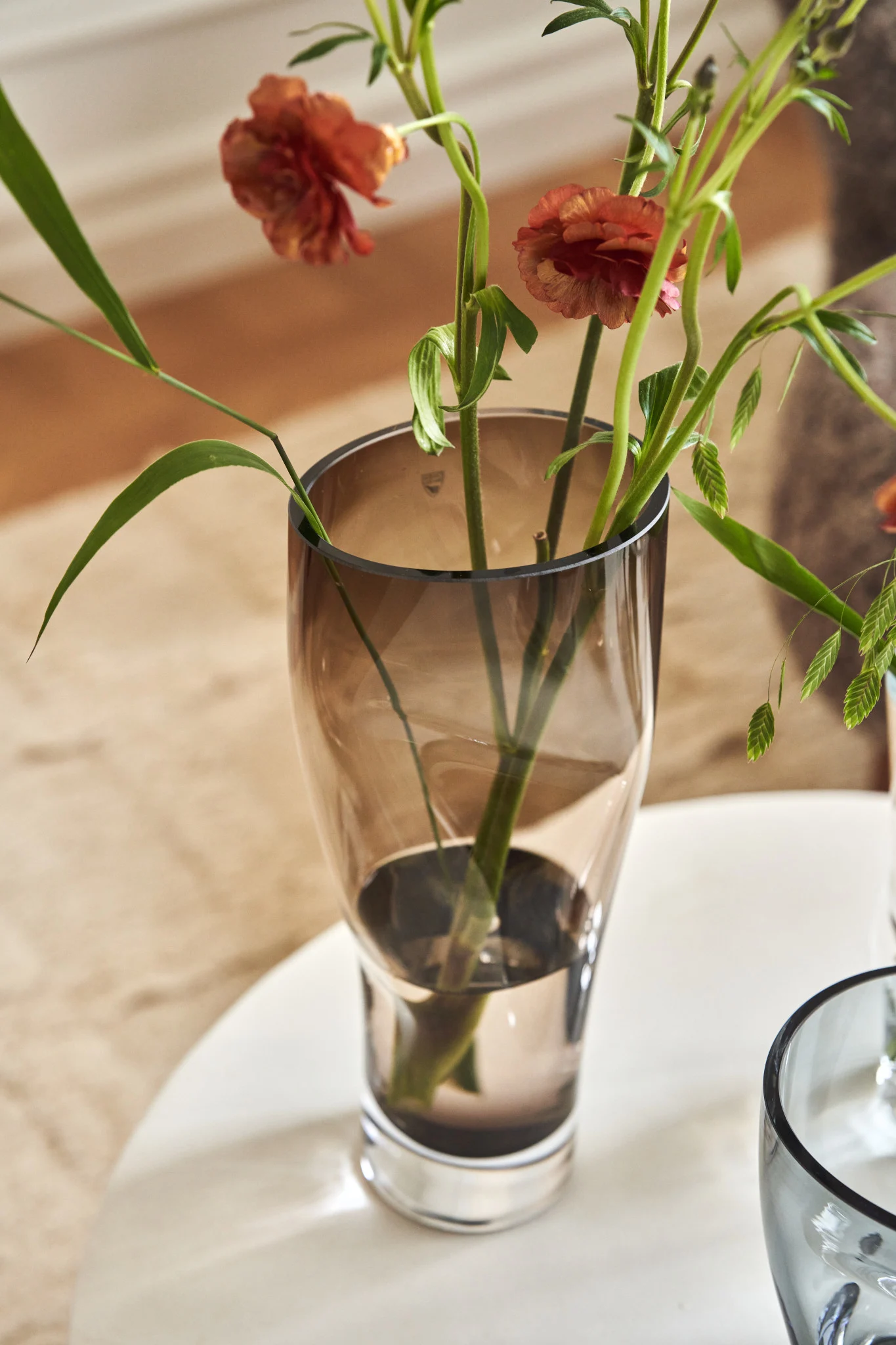 Auf einem Tisch steht die braune hohe Squeeze Vase von Orrefors mit Schnittblumen.