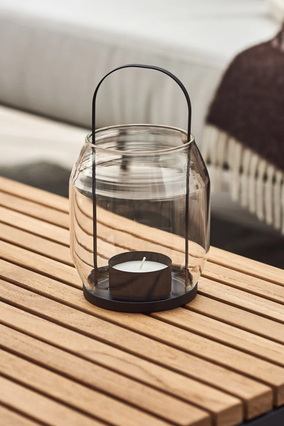 Lyhdyt ja myrskylyhdyt ulkotiloihin - tässä näet lasista ja mustasta metallista valmistetun ERNST-lyhdyn, joka seisoo puisella parvekepöydällä.