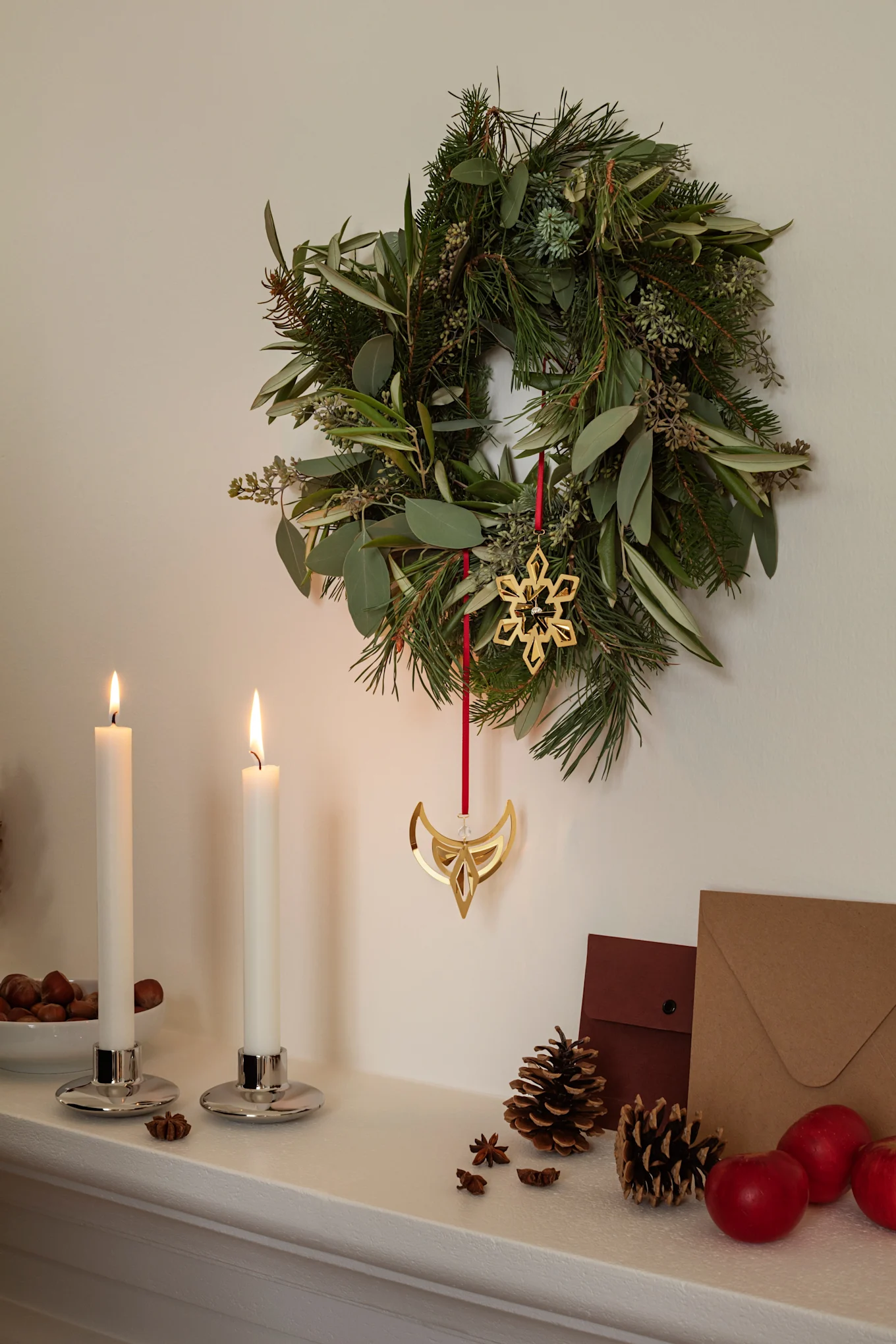 Ein Weihnachtskranz mit zwei Weihnachtsanhängern von Georg Jensen aus Messing, die einen Stern und einen Engel darstellen.