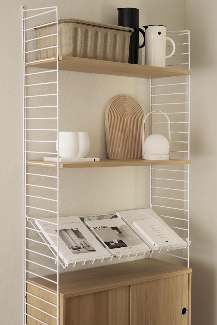 Das in Beige von @b.wohnbar dekorierte String Regal mit Ferm Living Boxen, der Carrie Tischlampe und einigen Zeitschriften.