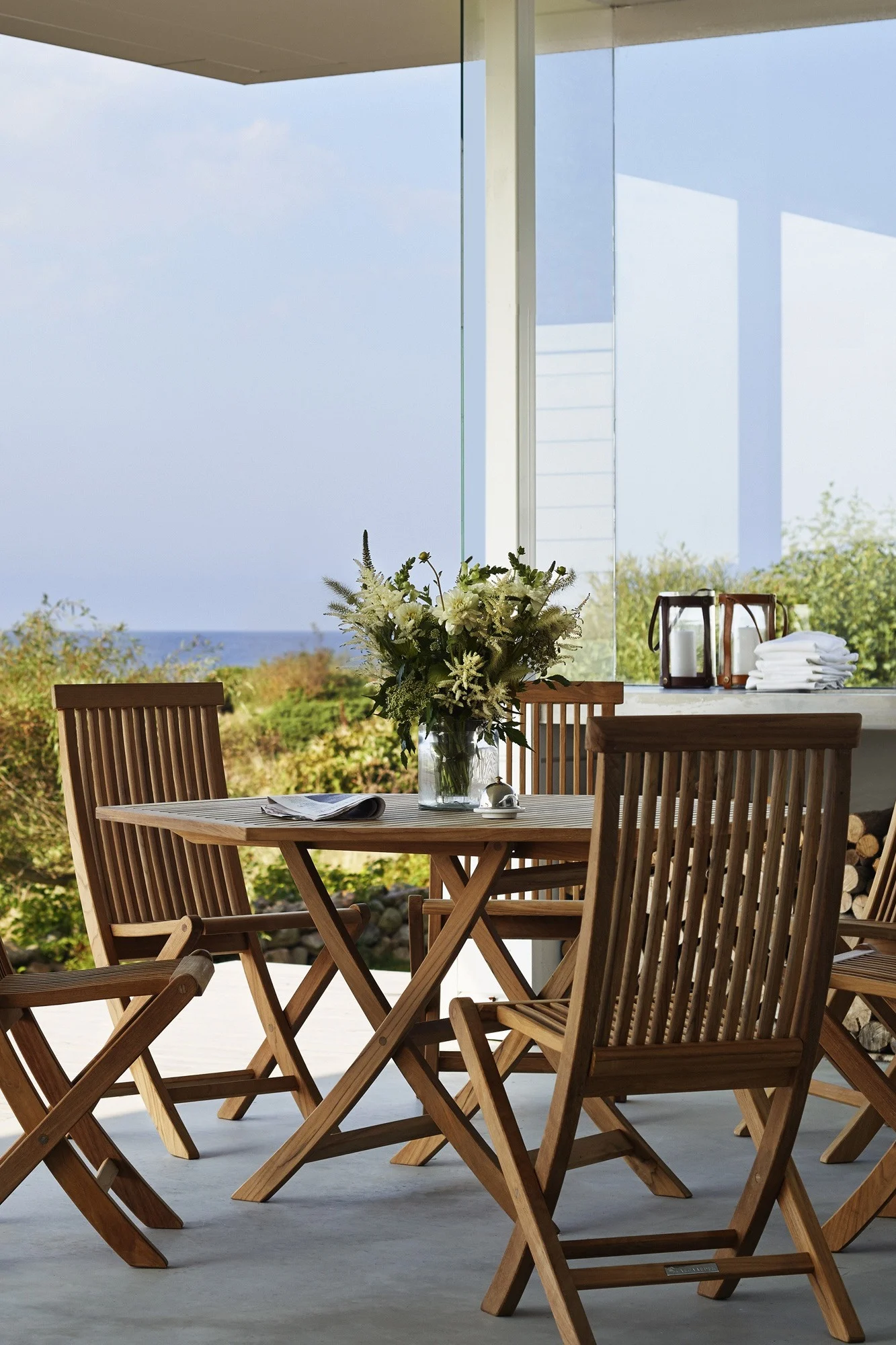 Teakholz ist ein Trend unter den Gartenmöbel-Trends 2025. Hier sehen Sie den Tisch und die Stühle aus der Viken-Kollektion von Skargaarden auf einer Terrasse stehen.