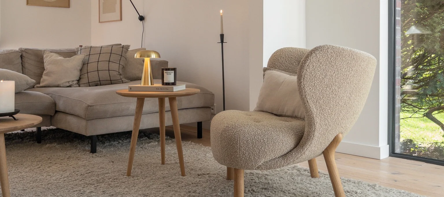 Das Wohnzimmer in Beige von haus_tannenkamp mit beigefarbener Couch, beigefarbenem Teppich, hellen Holzmöbeln und dem Little Petra Sessel von &Tradition.