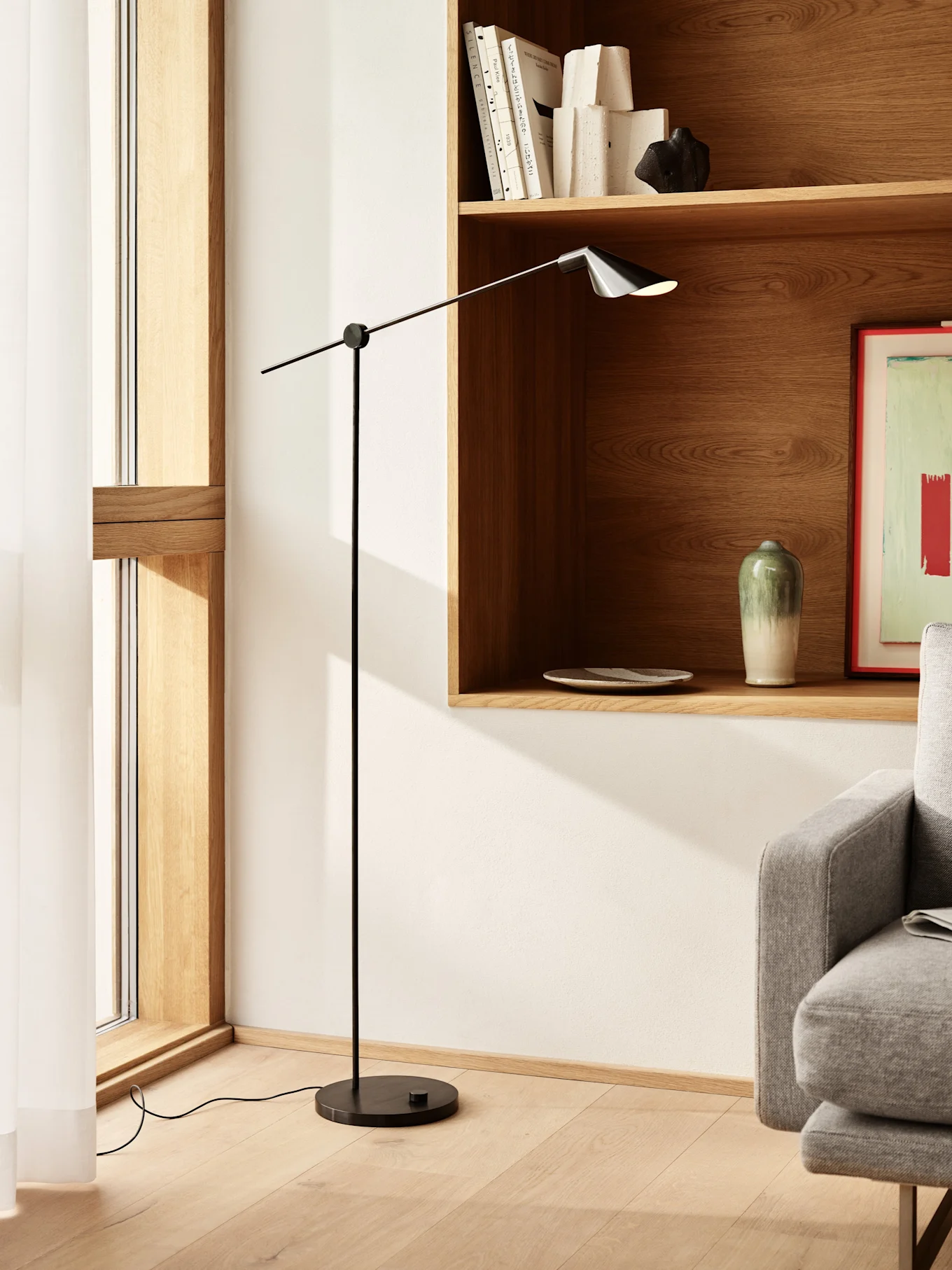 Hohe, schlanke schwarze Stehlampe mit verstellbarem Arm und dunklem Schirm in einem modernen Wohnraum mit Holzregalen.